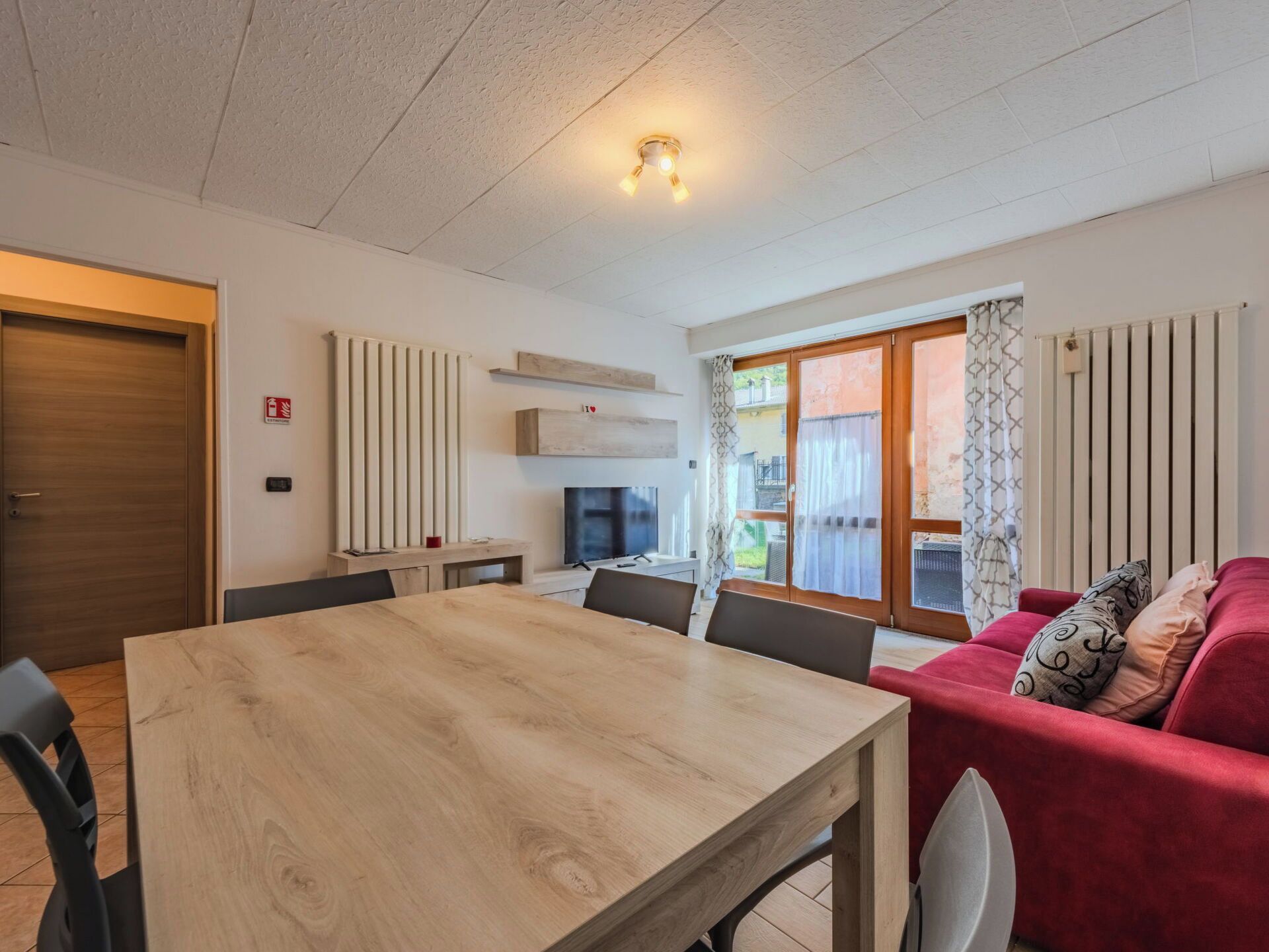 Una sala moderna con una mesa de comedor de madera, un sofá rojo y una televisión.