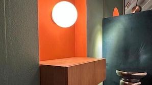 A modern bathroom with a wooden bench, a round light fixture, and a metallic stool.