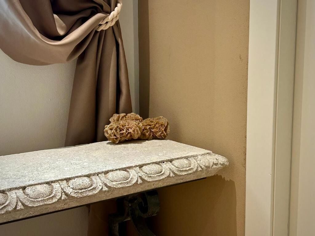 Esquina de una habitación con un repisa de piedra texturizada y un nudo decorativo en una cortina.