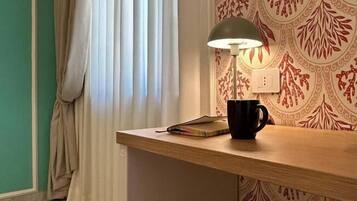 Ein Zimmer mit einem Holztisch, einer Lampe, einer schwarzen Tasse und einem gemusterten Wandteppich.