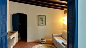 A room with a white sofa, a small round rug, a framed seahorse artwork, and a wooden ceiling.