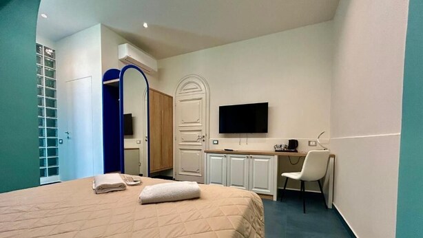 A hotel room with a bed, a desk, a chair, a television, and a wardrobe.