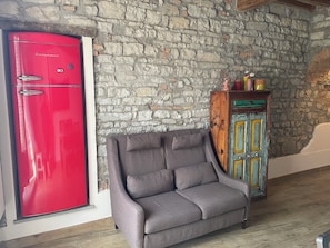 A room with a stone wall, a red appliance, a grey sofa, and a colorful cabinet. - A charming two-room apartment surrounded by greenery on a farm just a short walk from the city (sesto fiorentino)