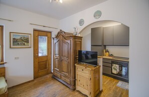 A room with a wooden wardrobe, a television on a wooden cabinet, a kitchen area with cabinets, and a painting on the wall. - Ground floor flat with a small terrace in the heart of San Vito di Cadore (San Vito di Cadore)