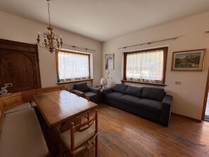 A cozy living room with a wooden dining table, a dark sofa, and a chandelier. - Ground floor flat with a small terrace in the heart of San Vito di Cadore (San Vito di Cadore)
