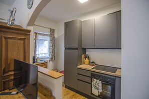 Eine kompakte Küche mit Backofen, kleiner Arbeitsfläche und einem Fenster mit gemusterten Vorhängen.