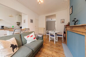 A modern living room with a sofa, a dining table with chairs, a kitchen area with a coffee machine, and a blue accent wall. - Central Easy Acces Self Check in 2 Room Venue (Brussels)