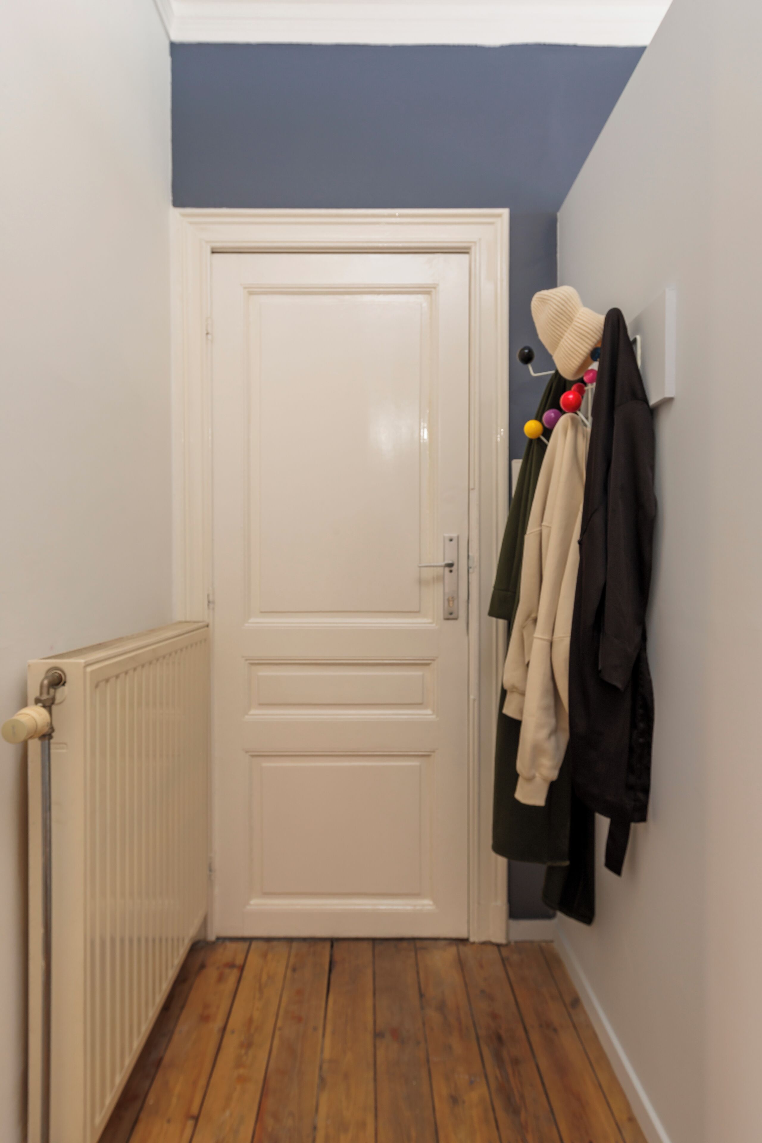 A hallway with a white door, a radiator, and a coat rack with various garments.