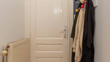 A hallway with a white door, a radiator, and a coat rack with various garments.