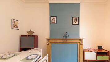 A dining area with a table set for two, a fireplace, and framed pictures on the wall.