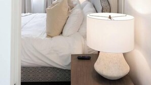 Et hotelværelse med seng, sengetøj, lampe, natbord og et vindue med gardiner.