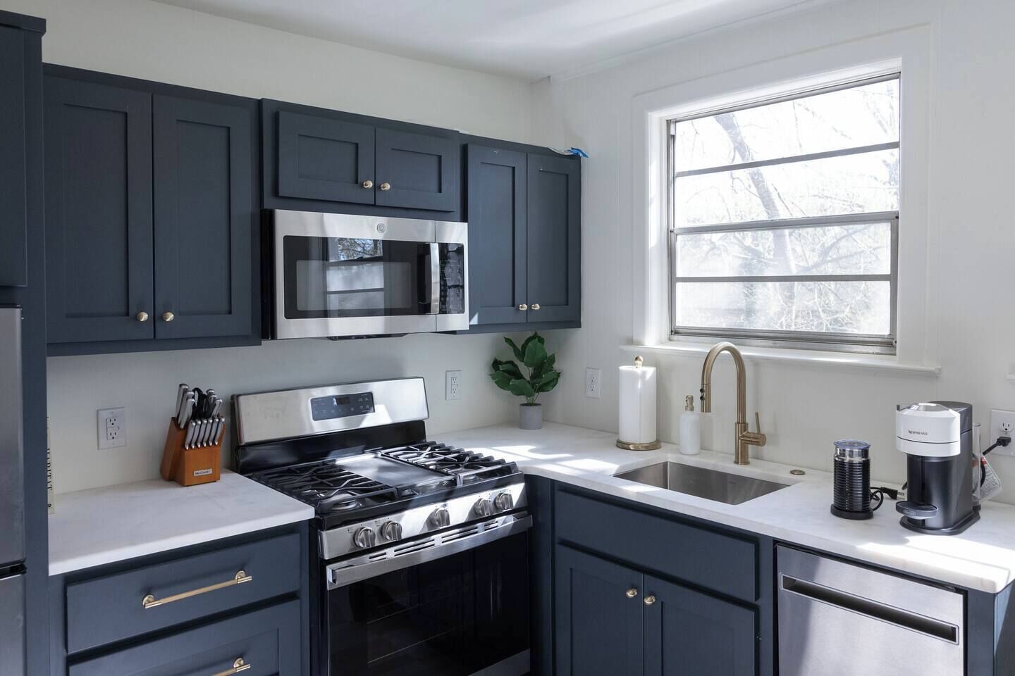 A modern kitchen with dark cabinets, stainless steel appliances, a gas stove, a microwave, and a window providing natural light.
