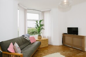 Un salon avec un canapé, un téléviseur posé sur un meuble, une plante en pot et une vue par la fenêtre.