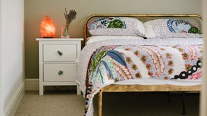 A bed with a floral quilt, a bedside table with a salt lamp, and a small drawer unit. - Stunning Apartment Near Fistral Beach (Newquay)