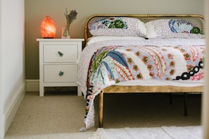 Ein Bett mit floraler Steppdecke, ein Nachttisch mit einer Salzlampen und eine kleine Kommode.