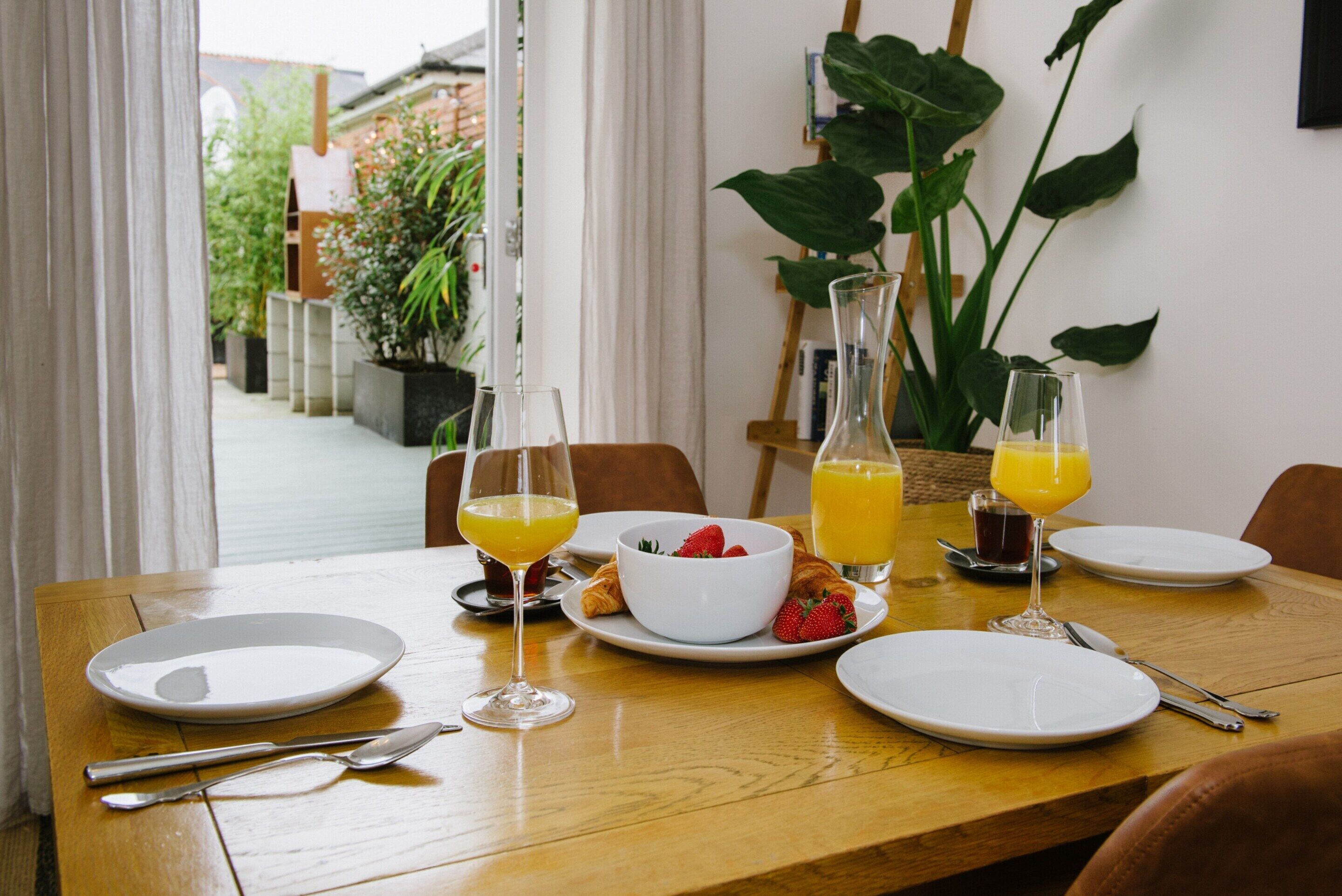 A breakfast table with plates, glasses, and a bowl of strawberries.