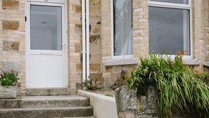 A stone building with a white door and two windows, a set of concrete stairs, and some greenery. - Stunning Apartment Near Fistral Beach (Newquay)