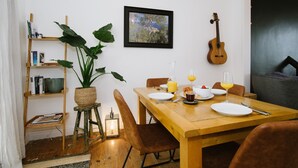 A dining area with a wooden table set for breakfast, a guitar, and a bookshelf with books and a plant. - Stunning Apartment Near Fistral Beach (Newquay)
