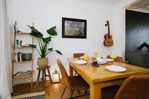 A dining area with a wooden table set for breakfast, a guitar, and a bookshelf with books and a plant.