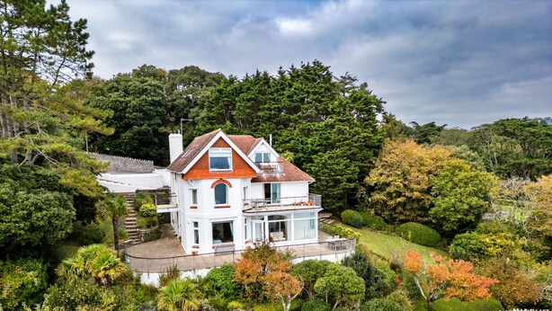 Ein zweistöckiges Haus mit Balkon, umgeben von üppigem Grün und Bäumen.