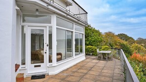 Eine überdachte Terrasse mit Glasveranda, einem Holztisch und Stühlen.