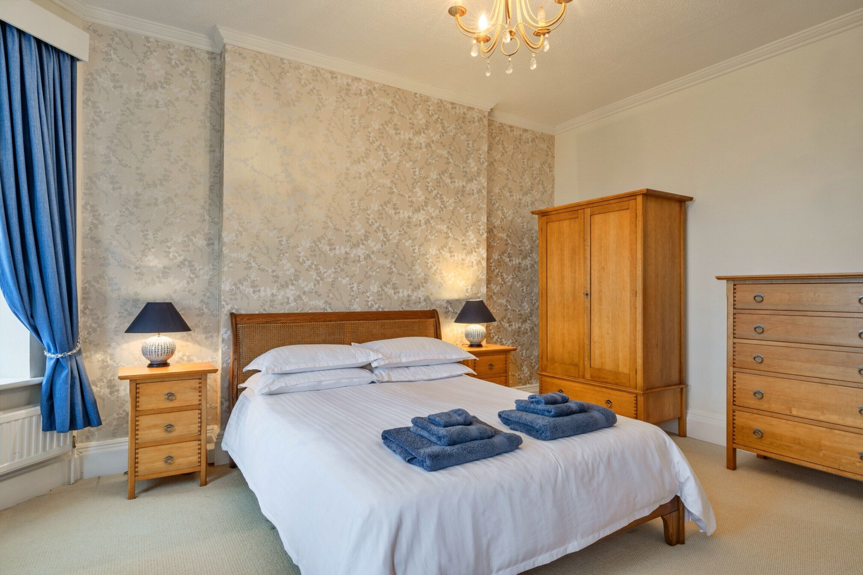 Um quarto com uma cama grande, duas mesas de cabeceira com abajures, um guarda-roupa de madeira e uma cortina azul.