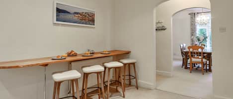Una cocina con barra de madera, cuatro taburetes, una mesa de comedor con sillas y un cuadro en la pared.