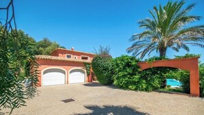 A two-story house with a red-tiled roof, two garage doors, a swimming pool, and lush greenery. - Villa 'Maison Rouge - Esprit Du Sud' with Sea View, Private Pool and Wi-Fi (Sainte-Maxime)