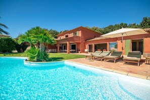 Uma casa de dois andares com piscina, cadeiras de descanso ao ar livre e uma palmeira.