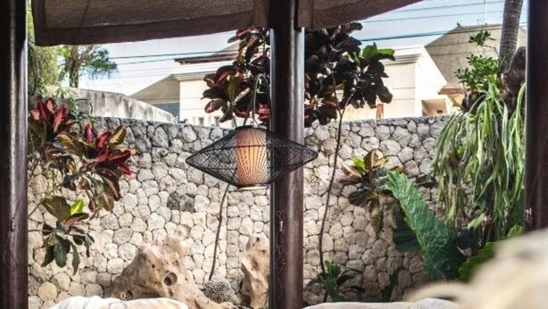 An outdoor seating area with a stone wall backdrop, a hanging lantern, and various plants. - Sandi Kala Villas - Two-Bedroom Villa (Badung Regency)