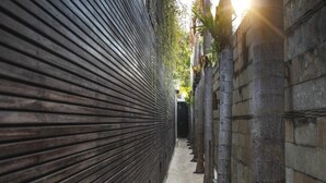 A narrow corridor with a closed shutter on one side and a columned wall on the other. - Sandi Kala Villas - Two-Bedroom Villa (Badung Regency)