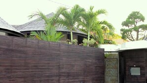 A modern house with a wooden exterior wall, a metal gate, and a small garden area. - Sandi Kala Villas - Two-Bedroom Villa (Badung Regency)