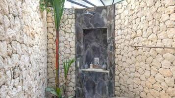 Een buitengebied met stenen muren en een glazen deur naar een douche, omringd door tropische planten.
