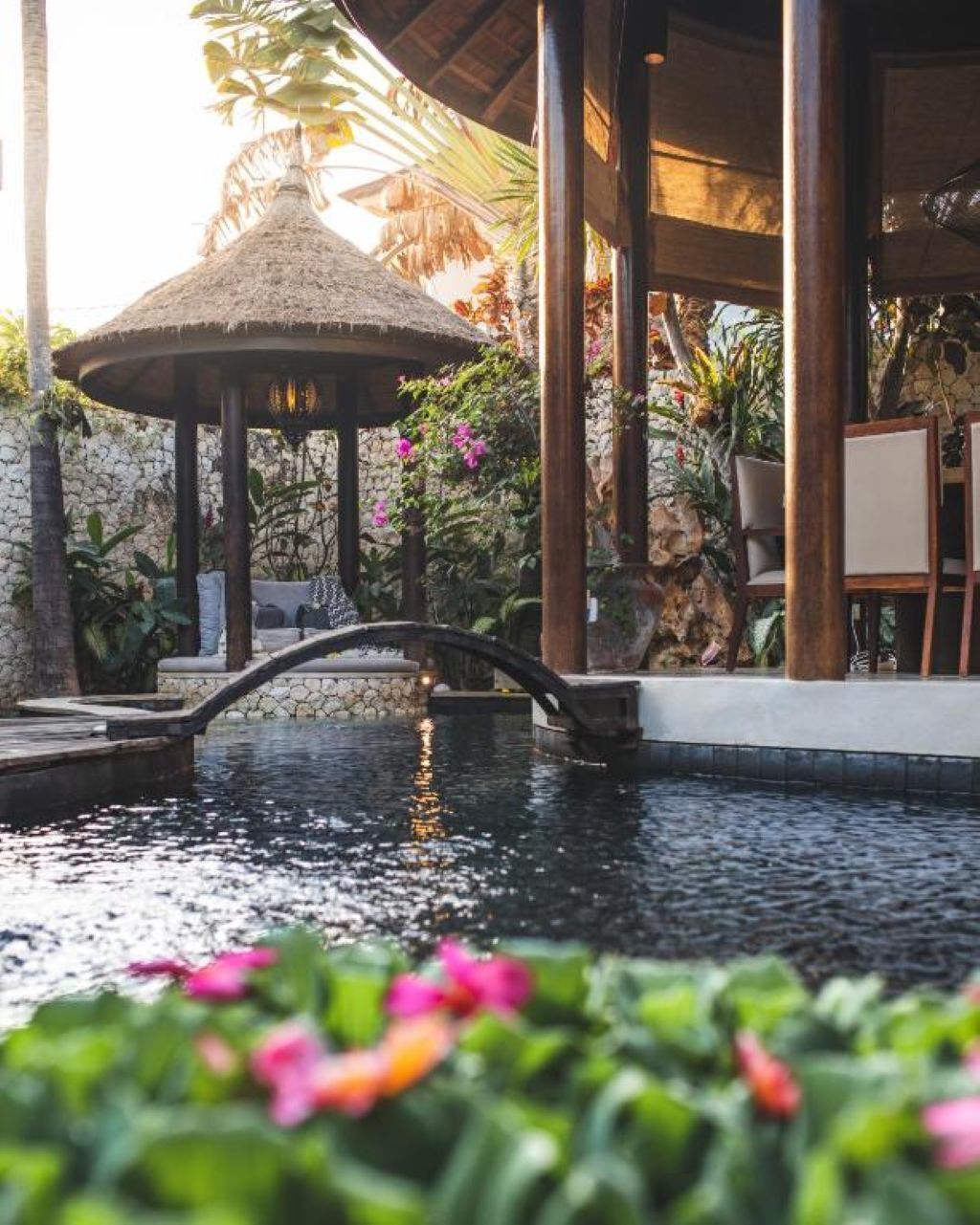 A tranquil outdoor area with a water feature, a thatched gazebo, and lush greenery.
