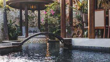 A tranquil outdoor area with a water feature, a thatched gazebo, and lush greenery.
