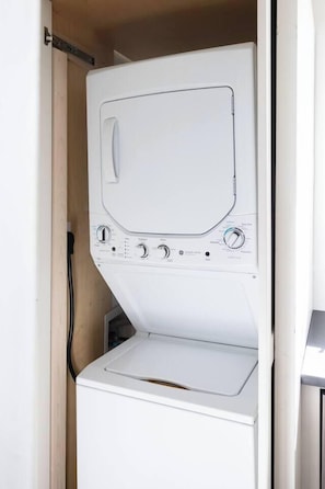 A white washing machine with control knobs and a door, installed in a wooden cabinet. - Excellent 1BR · Near Fort Jackson & Devine St (Columbia)