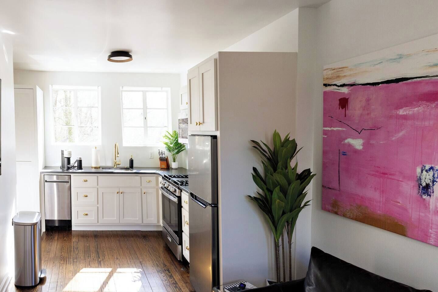A modern kitchen with white cabinetry, stainless steel appliances, and a large window providing natural light.