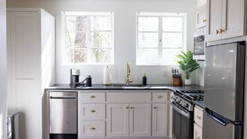 A kitchen with white cabinets, a stainless steel refrigerator, a dishwasher, and a double sink.