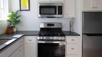 A kitchen with white cabinets, stainless steel appliances, and a dark wooden floor.