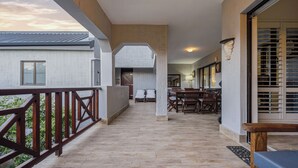 A spacious balcony with a wooden railing, a tiled floor, and a view of the sky.