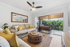 A modern living room with a sofa, coffee table, and a ceiling fan. - Paradise Beach Apartment | Pool | Ballito (Dolphin Coast)