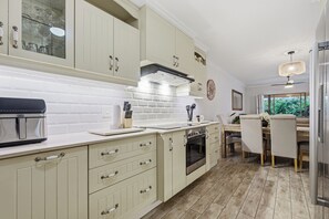 A kitchen with white cabinets, a built-in oven, and a dining area with a table and chairs. - Paradise Beach Apartment | Pool | Ballito (Dolphin Coast)