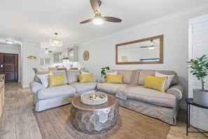 A modern living room with a sectional sofa, a coffee table, and a ceiling fan. - Paradise Beach Apartment | Pool | Ballito (Dolphin Coast)
