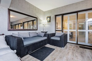 A modern living room with a sofa, armchairs, a large mirror, and a view through a sliding glass door. - Paradise Beach Apartment | Pool | Ballito (Dolphin Coast)