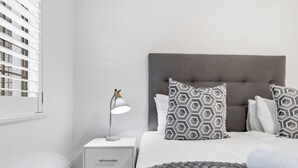 A bedroom with a bed, a bedside table with a lamp, and a window with blinds.
