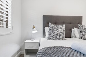 A bedroom with a bed, a bedside table with a lamp, and a window with blinds.