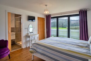 A bedroom with a bed, a vanity with a mirror, a shower, and a television on the wall. - Westward Ho Seaside Stay ( (Bideford)
