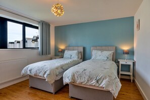 A bedroom with two single beds, a window, and a hanging light fixture. - Westward Ho Seaside Stay ( (Bideford)