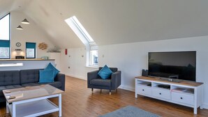 A modern living room with a sofa, armchair, coffee table, TV, and a dining area with a microwave. - Westward Ho Seaside Stay ( (Bideford)