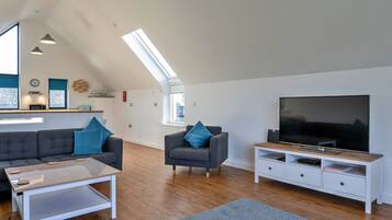 A modern living room with a sofa, armchair, coffee table, TV, and a dining area with a microwave.